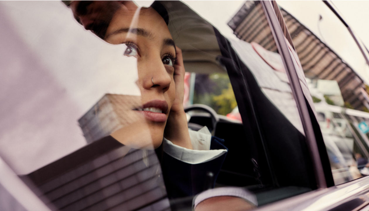 Woman looking out of car window with slight reflection on glass.
