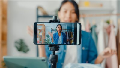 A phone on a tripod showing a woman recording herself talking to the camera.