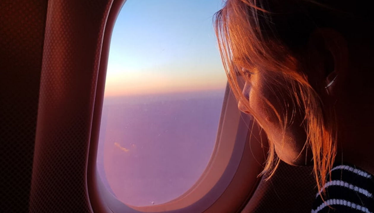 Eine Frau, die sich aus einem Flugzeugfenster den Sonnenuntergang anschaut