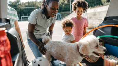 A mother and her two children loading their dog into the car for a trip.