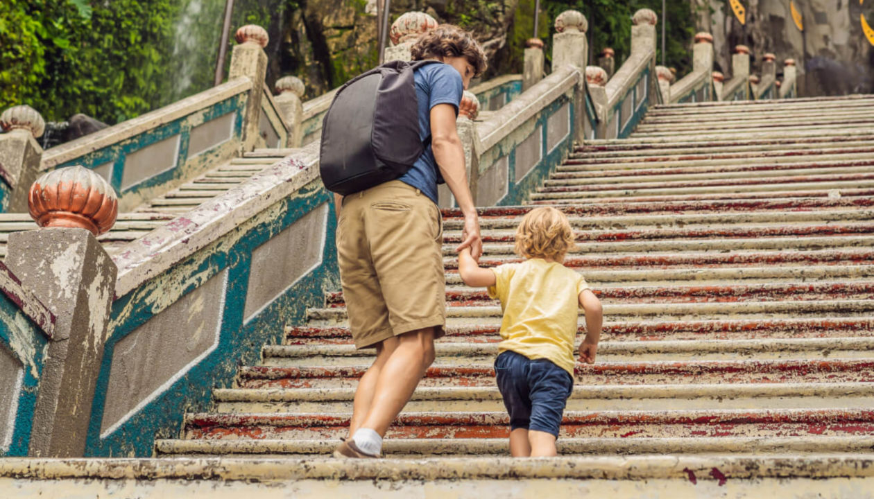 A man holds the hand of his child as they walk up stairs
