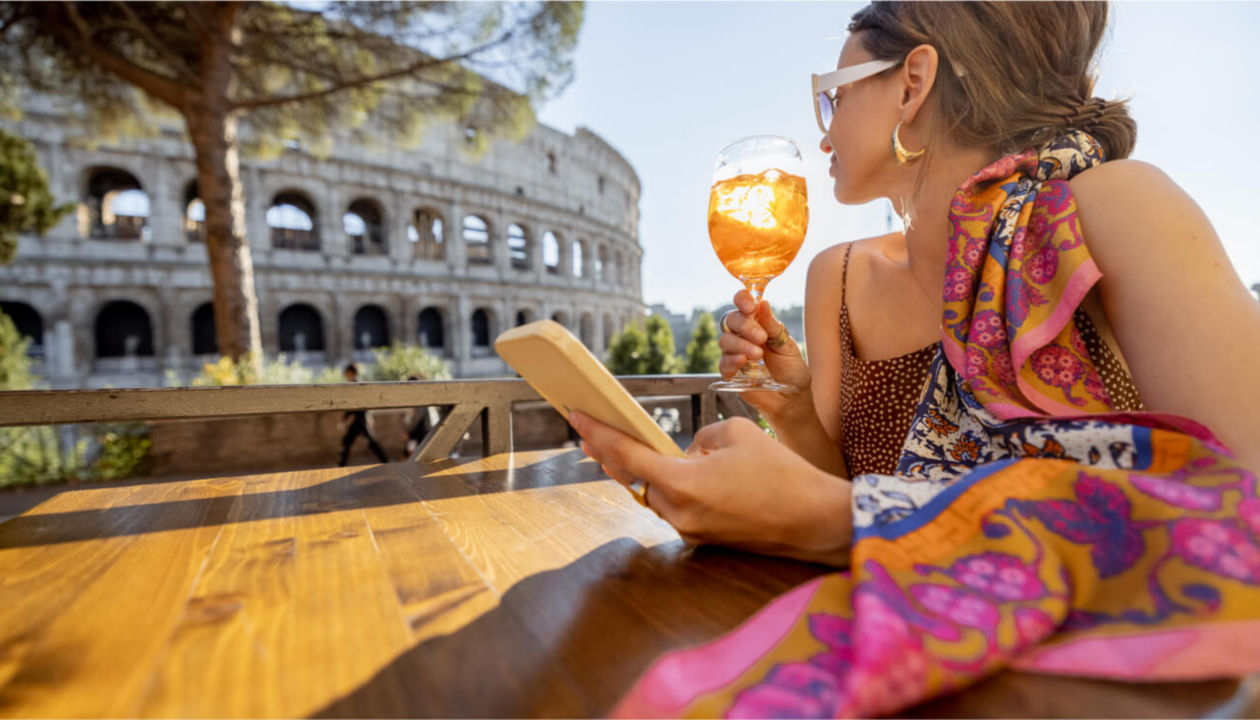 Donna con un drink in mano che guarda il cellulare di fronte al Colosseo