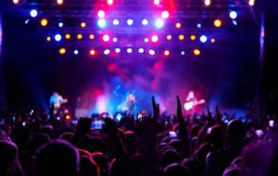Una gran multitud en un concierto con luces de colores y artistas sobre el escenario.