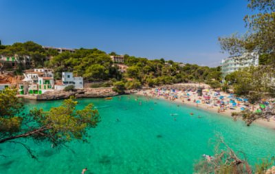 Playa bulliciosa rodeada de exuberante vegetación y agua turquesa, llena de bañistas.