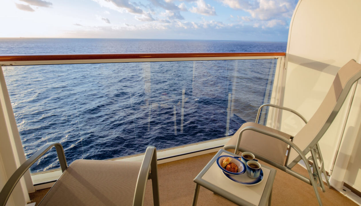 Der Balkon einer Luxuskabine mit Meerblick und einem kleinen Tisch mit Frühstücksspeisen 