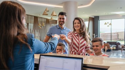 Young family with two children smiling as a receptionist hands over room keys at a modern hotel front desk