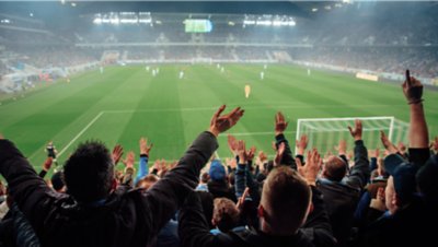 Diverse group of enthusiastic fans raising their hands, celebrating in packed stadium seating