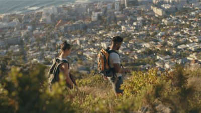 Ein Latinx-Paar wandert entlang eines sonnigen Bergrückens mit Blick auf eine Stadtlandschaft