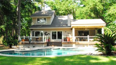 A house surrounded by trees and with a pool in front of it