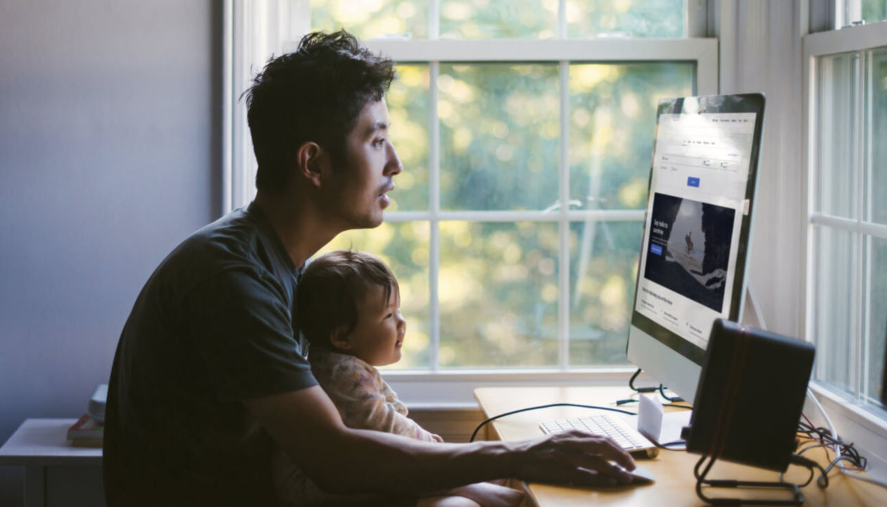 A man browsing the internet with an infant sitting on his lap
