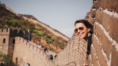 Viajante de férias em um destino colocando a cabeça pra fora em um vão da Grande Muralha da China.