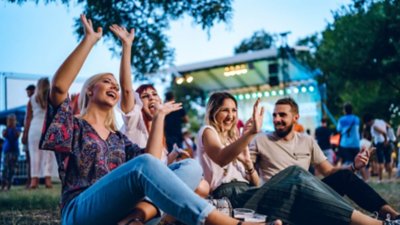 Group of friends sitting on a lawn enjoying an outdoor afternoon concert together.