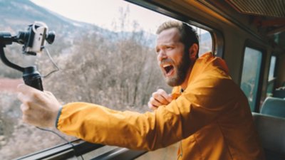 Hombre en un tren grabando su experiencia de viaje para promocionar plataformas de viajes de ocio y negocios en su blog.