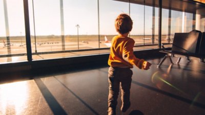 Criança no aeroporto correndo para observar os aviões na pista através do vidro enquanto espera o seu voo.