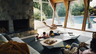 A family relaxes in a vacation rental, with the parents sitting on a sofa while their two children play a game laying on the floor.