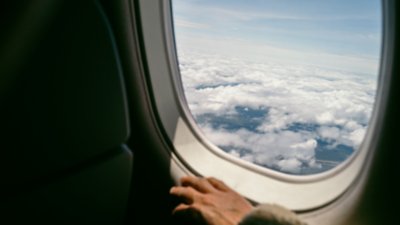 A sky view from inside an airplane with an arm resting near the window.