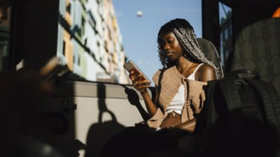 A woman sits on a bus, commuting through a city while looking at her phone.