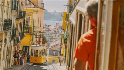 The famous yellow Tram 28 climbs a hill in a scenic area of Lisbon, Portugal.