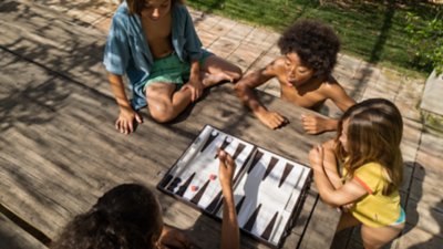 Un groupe de quatre enfants qui jouent à un jeu de société autour d’une table en bois dans un jardin