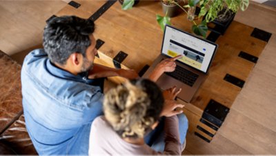 Two people at a table looking at a laptop together, while person on the left is pointing at the laptop screen