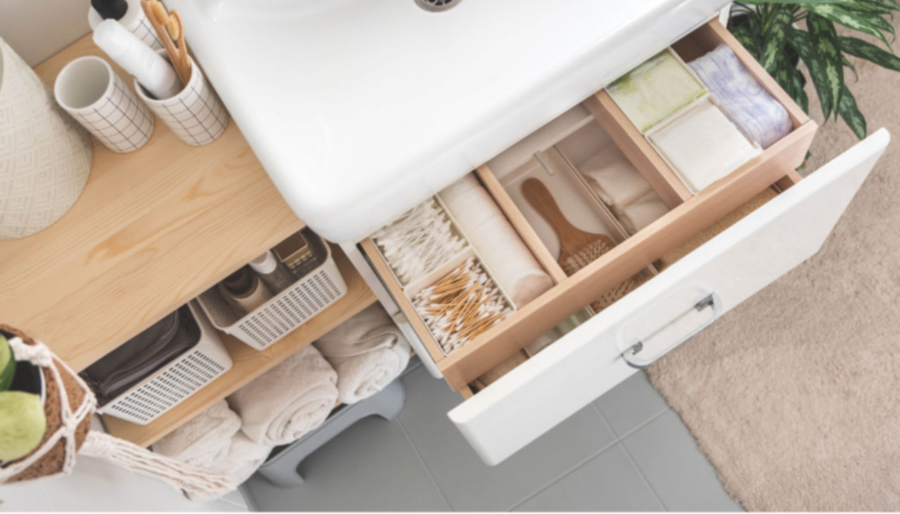 Bathroom drawers with neatly placed bath amenities and toiletries. Shelf storage with liquid soap dispenser and rolled up white towels.