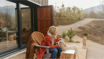 Eine Frau und ein Hund sitzen auf einer Terrasse vor einem Haus