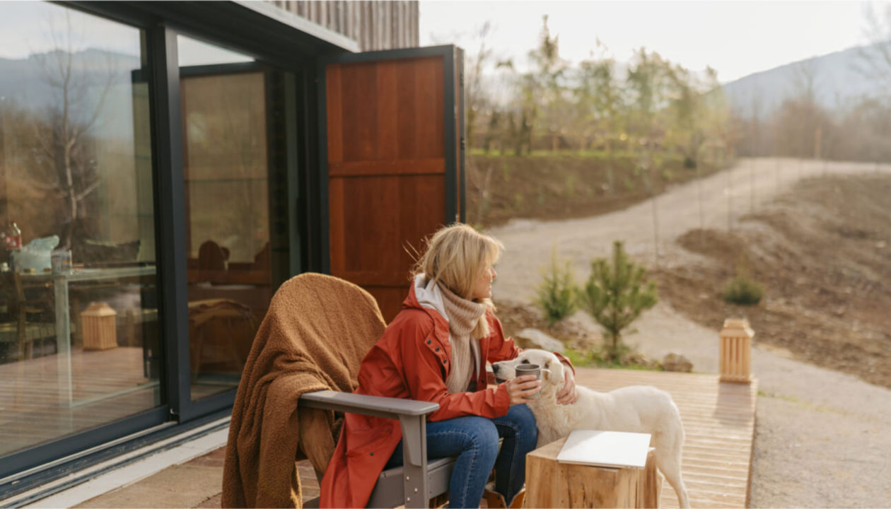 Eine Frau und ein Hund sitzen auf einer Terrasse vor einem Haus