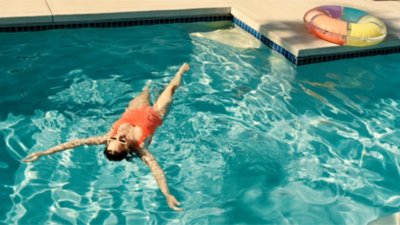  Woman in a red swimsuit floating on her back in a clear blue pool next to colorful inflatable rings.g